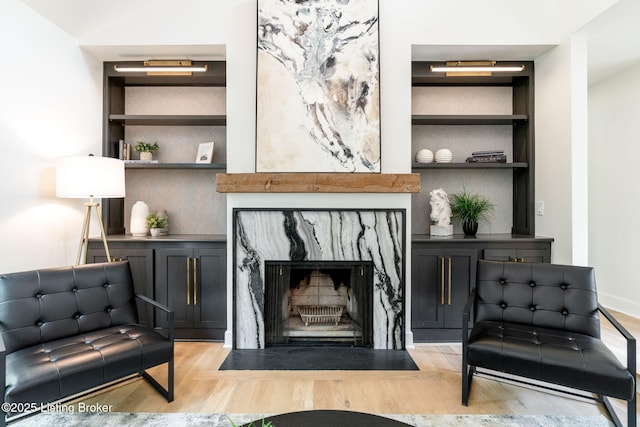 living room with built in shelves, a high end fireplace, and light hardwood / wood-style flooring