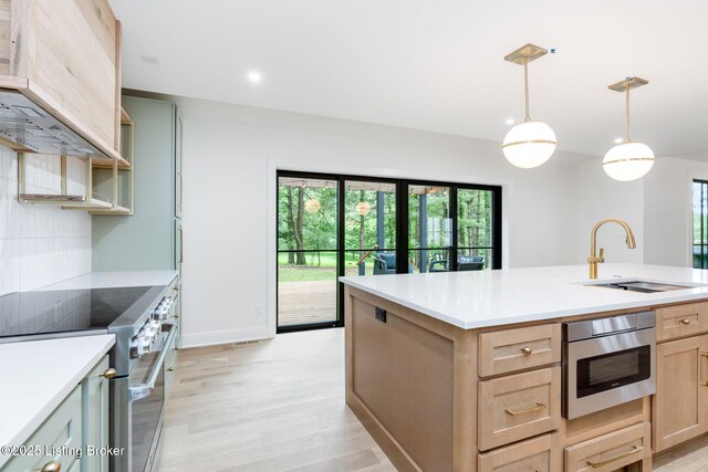 kitchen with appliances with stainless steel finishes, light brown cabinetry, sink, hanging light fixtures, and a kitchen island with sink