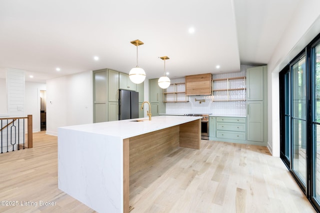 kitchen featuring pendant lighting, appliances with stainless steel finishes, a kitchen island with sink, light hardwood / wood-style floors, and decorative backsplash