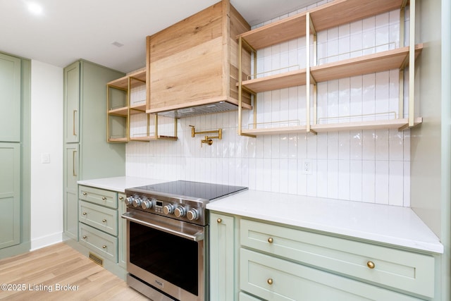 kitchen featuring premium range hood, tasteful backsplash, stainless steel range with electric stovetop, green cabinetry, and light wood-type flooring