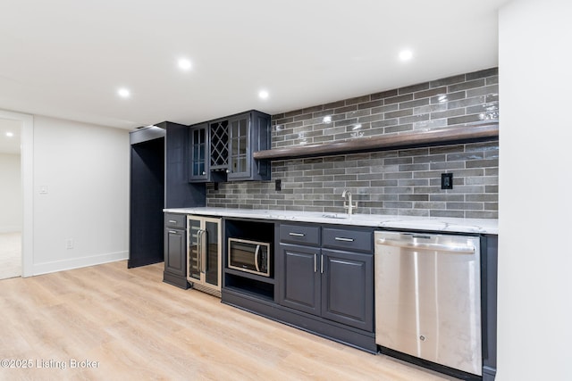 bar with appliances with stainless steel finishes, light stone counters, light hardwood / wood-style floors, decorative backsplash, and beverage cooler