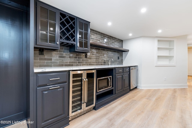 bar featuring appliances with stainless steel finishes, sink, wine cooler, decorative backsplash, and light hardwood / wood-style floors