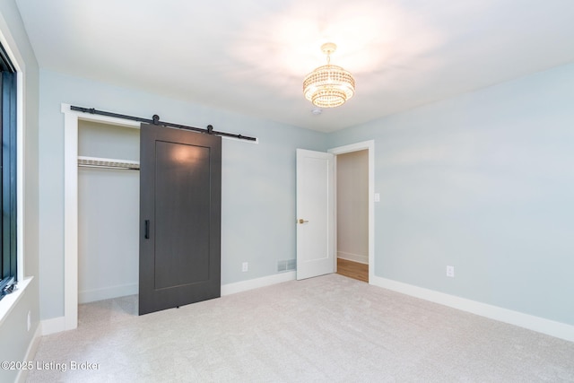 unfurnished bedroom featuring a barn door, light carpet, and a closet