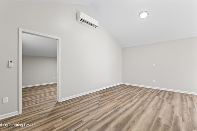 spare room featuring lofted ceiling, light wood-type flooring, and an AC wall unit