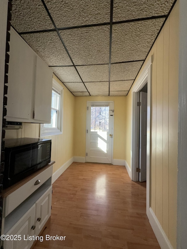 entryway featuring a drop ceiling, wooden walls, and light wood-type flooring