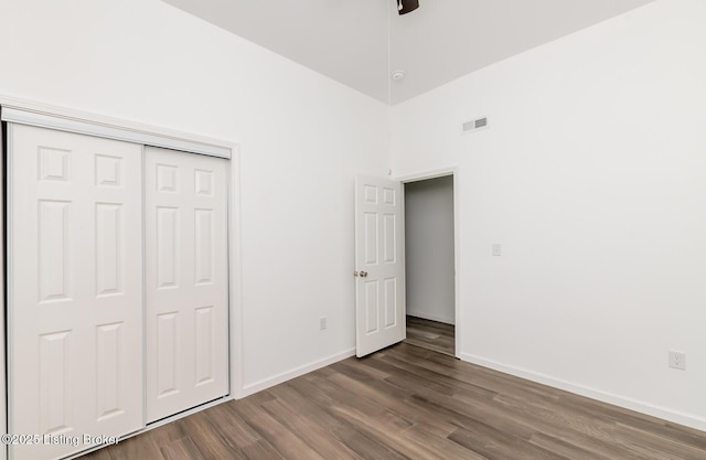 unfurnished bedroom with a towering ceiling, dark wood-type flooring, and a closet