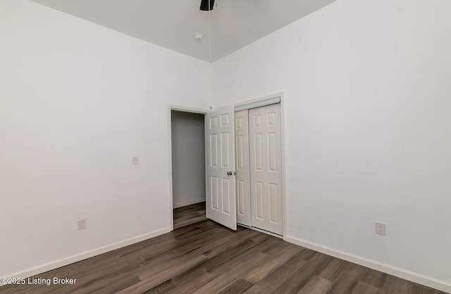 unfurnished bedroom with dark wood-type flooring, a closet, ceiling fan, and a high ceiling