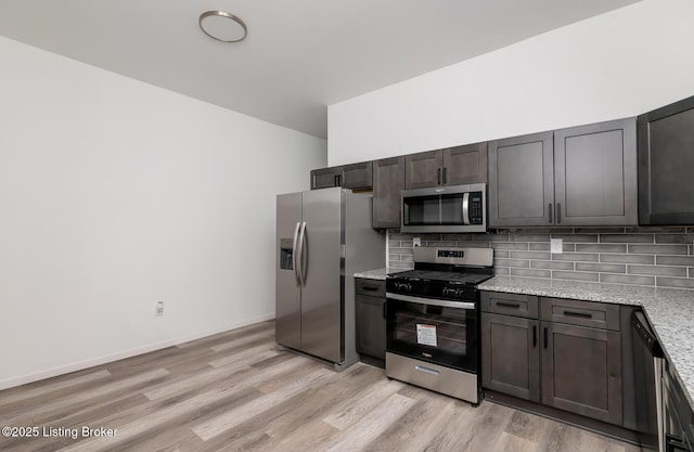 kitchen featuring appliances with stainless steel finishes, dark brown cabinets, light stone counters, light hardwood / wood-style floors, and decorative backsplash