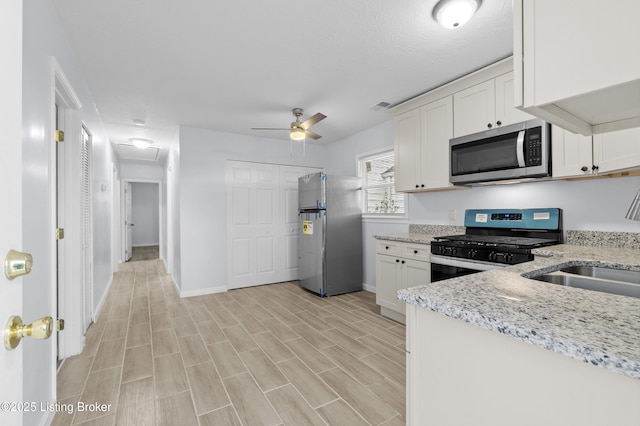 kitchen with light stone countertops, appliances with stainless steel finishes, white cabinets, and ceiling fan