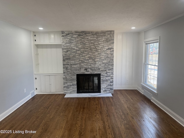 unfurnished living room featuring a stone fireplace, dark wood-type flooring, a textured ceiling, and built in shelves