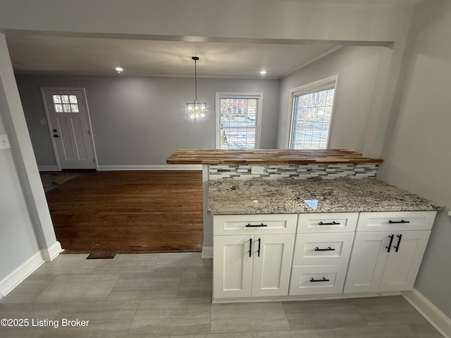 kitchen featuring decorative light fixtures, white cabinets, backsplash, kitchen peninsula, and light stone countertops