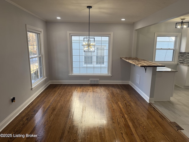 unfurnished dining area featuring a healthy amount of sunlight, dark wood-type flooring, and a chandelier