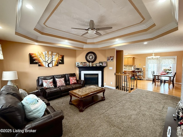 living room featuring a fireplace, ornamental molding, light colored carpet, ceiling fan, and a raised ceiling