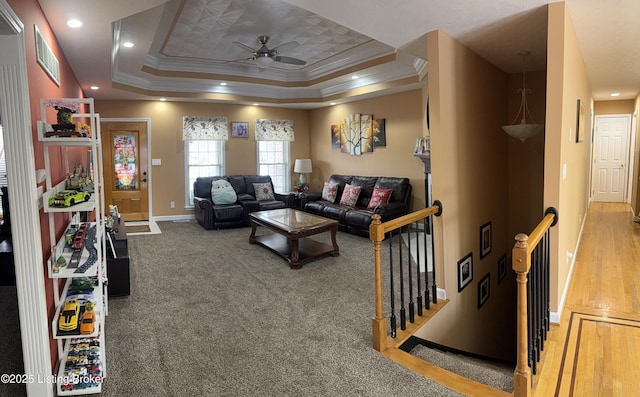 carpeted living room with ornamental molding, ceiling fan, and a tray ceiling