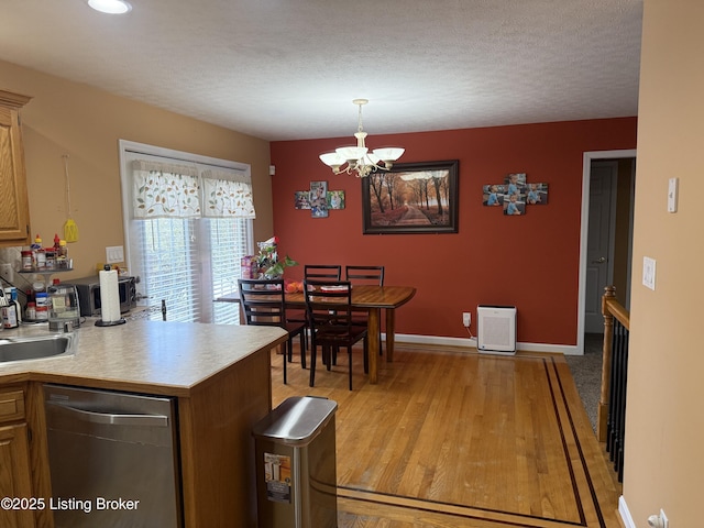 kitchen featuring pendant lighting, dishwasher, sink, a chandelier, and light hardwood / wood-style floors