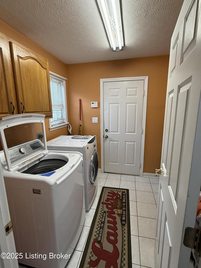 laundry area featuring cabinets, light tile patterned flooring, a textured ceiling, and washer and clothes dryer