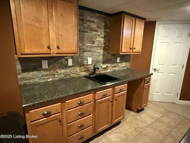 kitchen with sink, light tile patterned floors, dark stone countertops, decorative backsplash, and a drop ceiling