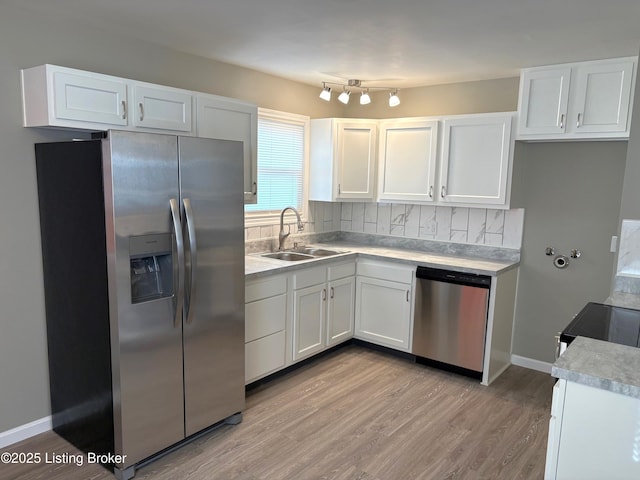 kitchen with appliances with stainless steel finishes, tasteful backsplash, white cabinetry, sink, and light hardwood / wood-style flooring