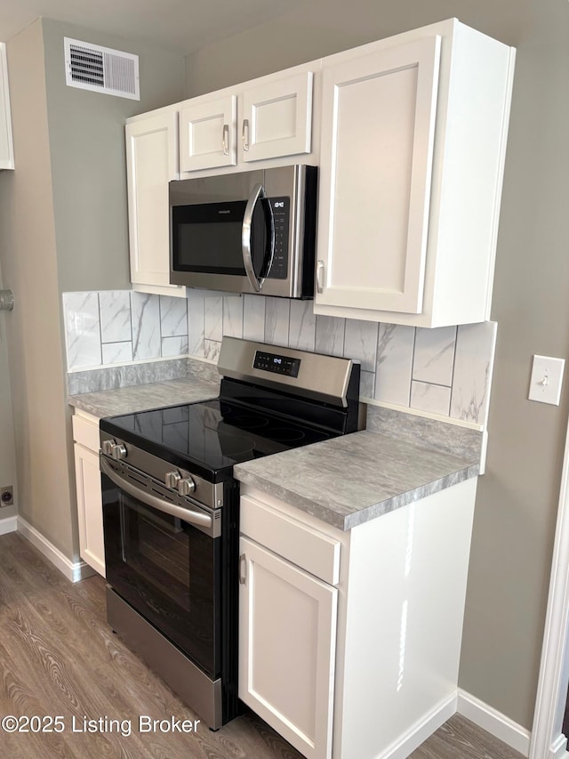 kitchen featuring white cabinetry, backsplash, wood-type flooring, and stainless steel appliances