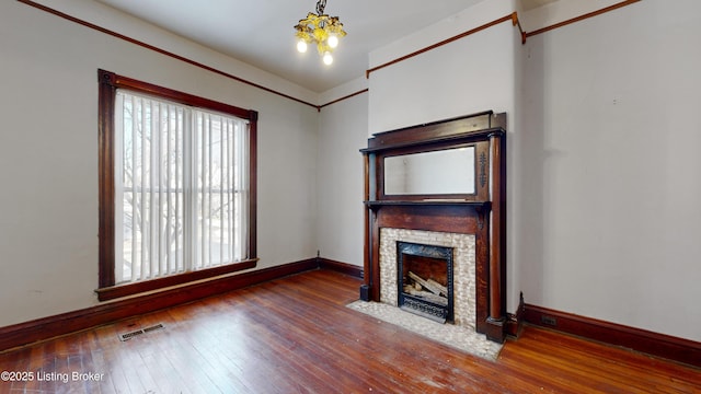 unfurnished living room with hardwood / wood-style flooring, a stone fireplace, and a notable chandelier