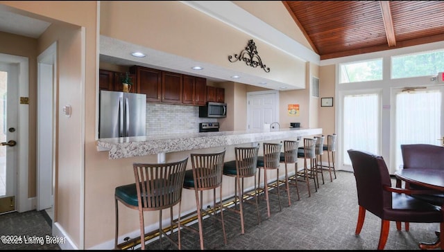 kitchen with stainless steel appliances, wood ceiling, a kitchen breakfast bar, and decorative backsplash