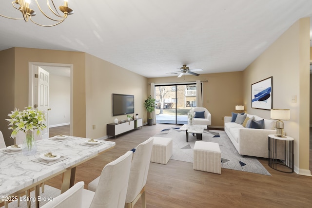 living room with ceiling fan with notable chandelier and light hardwood / wood-style flooring