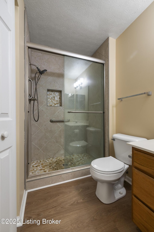 bathroom featuring hardwood / wood-style flooring, a shower with door, vanity, a textured ceiling, and toilet