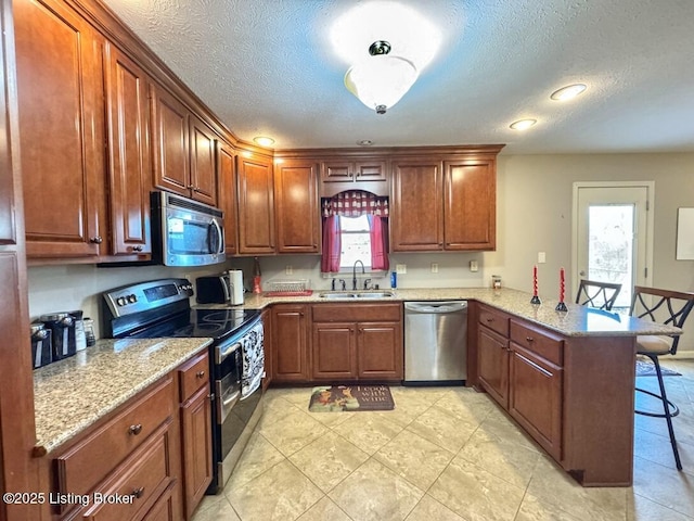 kitchen featuring a kitchen bar, sink, kitchen peninsula, stainless steel appliances, and light stone countertops