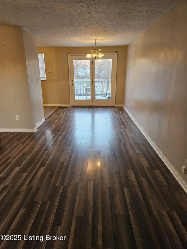 spare room with dark wood-type flooring, a textured ceiling, and an inviting chandelier