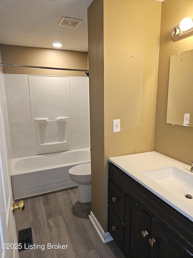 full bathroom with hardwood / wood-style floors, washtub / shower combination, vanity, toilet, and a textured ceiling