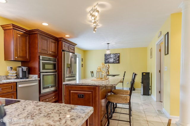 kitchen featuring a kitchen bar, ornate columns, decorative light fixtures, appliances with stainless steel finishes, and light stone countertops