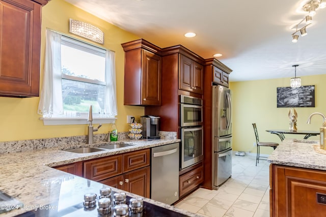 kitchen featuring light stone counters, stainless steel appliances, sink, and hanging light fixtures