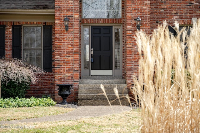 view of exterior entry featuring brick siding and roof with shingles