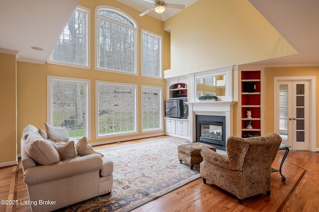 living room featuring a towering ceiling, a glass covered fireplace, crown molding, and wood finished floors