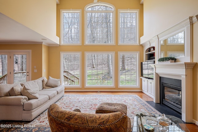 living room with wood finished floors, a fireplace with flush hearth, built in features, a towering ceiling, and crown molding