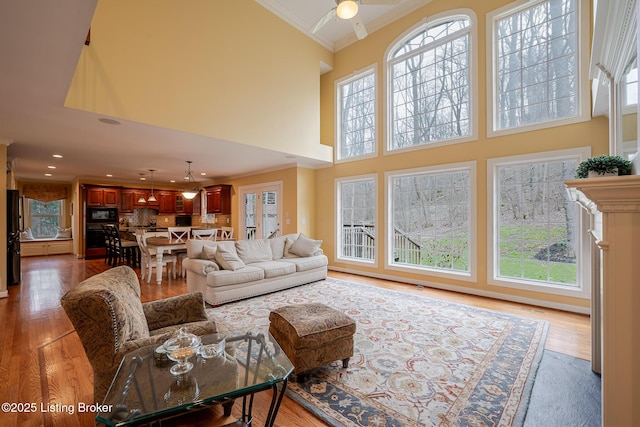 living area with a towering ceiling, ceiling fan, crown molding, and wood finished floors