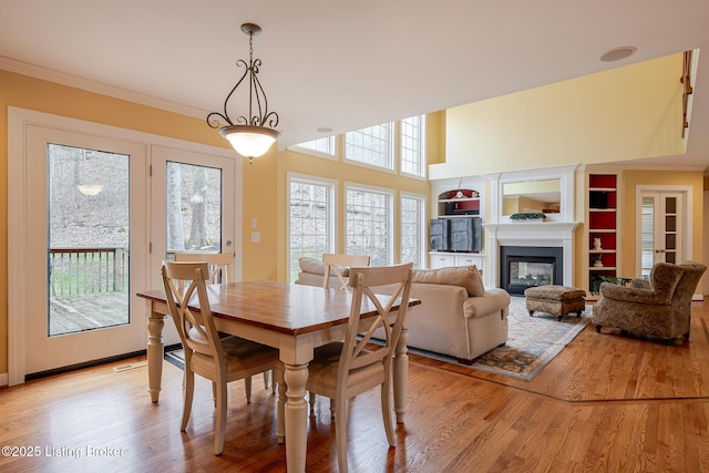 dining area featuring light wood finished floors, a high ceiling, crown molding, and a glass covered fireplace