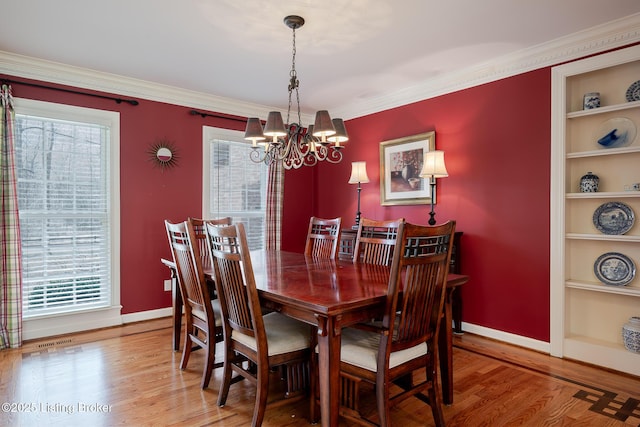 dining room with baseboards, ornamental molding, wood finished floors, built in shelves, and a notable chandelier