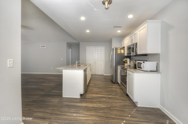 kitchen with stainless steel appliances, light stone countertops, a center island with sink, and white cabinets