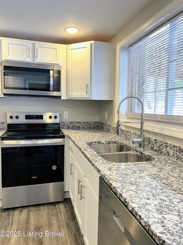 kitchen featuring dark wood-type flooring, sink, light stone counters, stainless steel appliances, and white cabinets