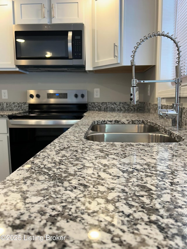 kitchen featuring white cabinetry, stainless steel appliances, sink, and light stone counters