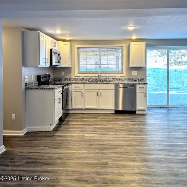 kitchen with stainless steel appliances, white cabinetry, and dark stone counters