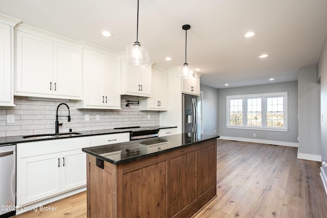 kitchen featuring sink, appliances with stainless steel finishes, hanging light fixtures, white cabinets, and dark stone counters