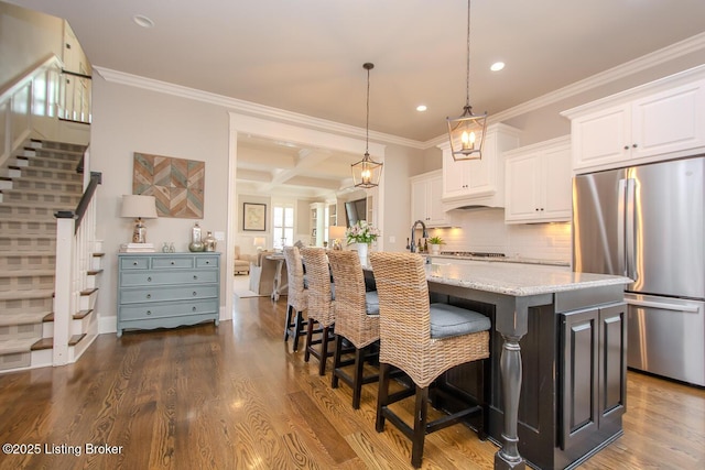 kitchen with stainless steel refrigerator, white cabinetry, coffered ceiling, and an island with sink