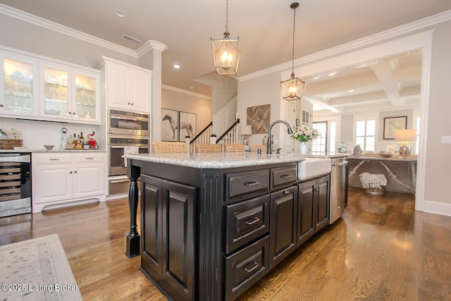 kitchen featuring white cabinetry, stainless steel appliances, light hardwood / wood-style floors, an island with sink, and beverage cooler