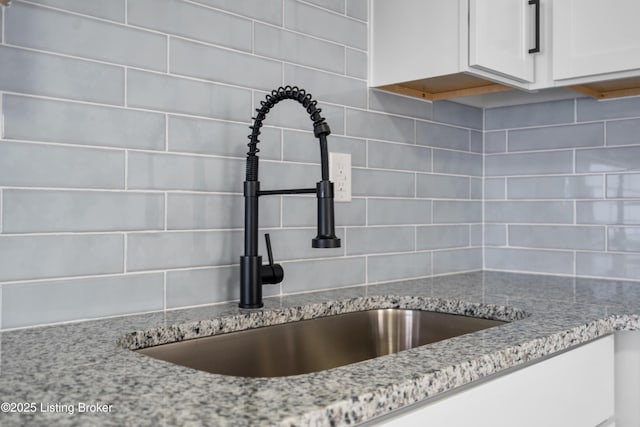 room details featuring tasteful backsplash, white cabinetry, light stone countertops, and sink