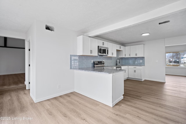 kitchen featuring appliances with stainless steel finishes, kitchen peninsula, white cabinetry, light hardwood / wood-style floors, and light stone counters