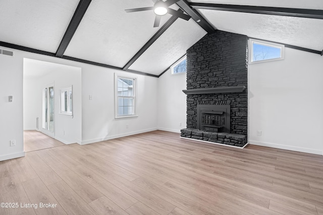 unfurnished living room featuring a stone fireplace, vaulted ceiling with beams, ceiling fan, light hardwood / wood-style floors, and a textured ceiling