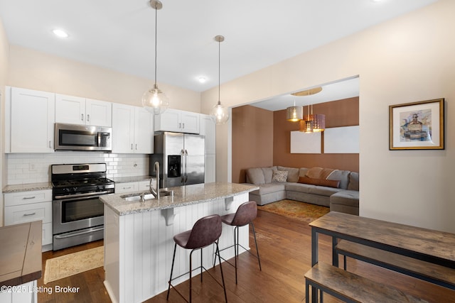 kitchen featuring sink, appliances with stainless steel finishes, white cabinetry, a kitchen island with sink, and light stone counters