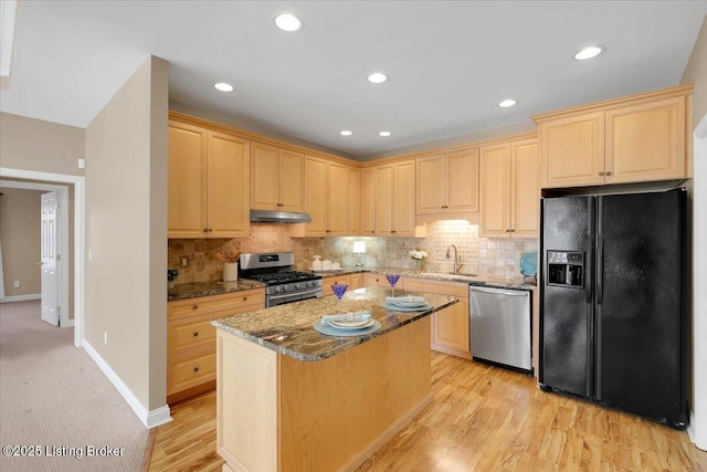 kitchen with appliances with stainless steel finishes, stone counters, light brown cabinetry, under cabinet range hood, and backsplash